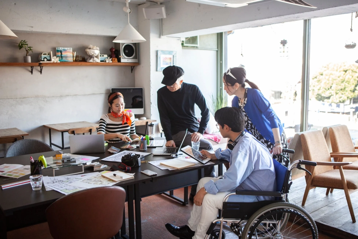 車椅子の男性を含む4人のチームが活発に打ち合わせをしている様子