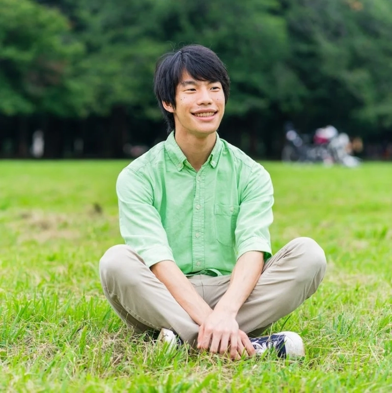 公園の芝生に座って笑顔を見せる若い男性