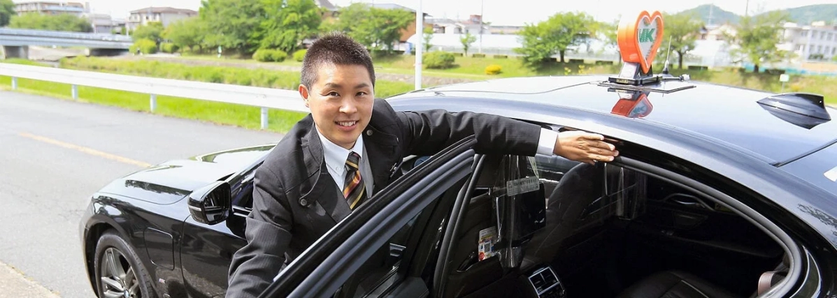 黒いタクシーの運転手が笑顔で車のドアを開けている