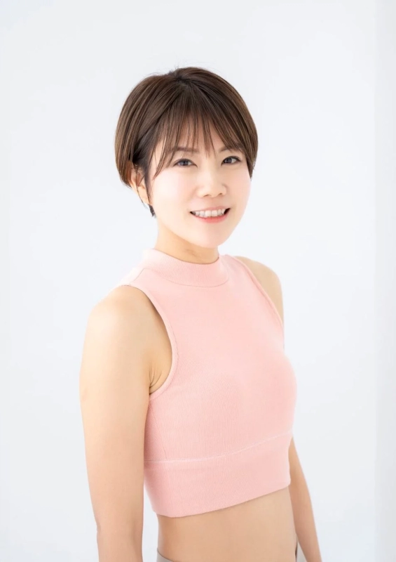 白い背景の前で、ピンクのノースリーブトップスを着たショートヘアの女性が笑顔でこちらを見ている