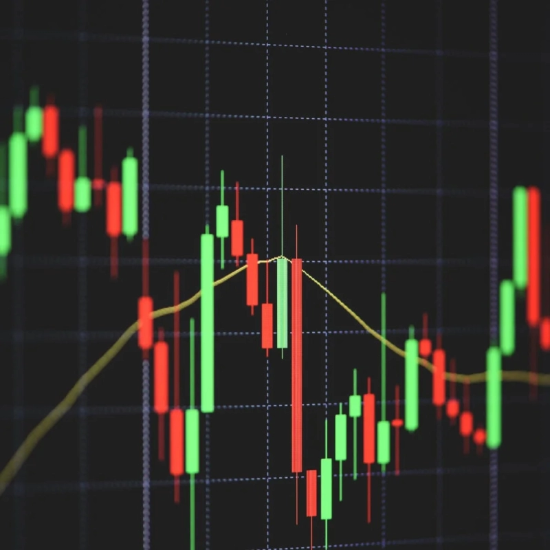 暗い背景にグリッド線が引かれた画面に、赤と緑のローソク足と黄色の移動平均線が表示された株価チャートです。