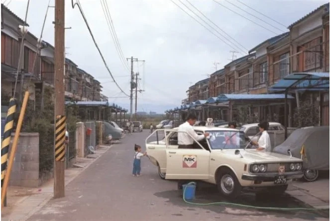 昭和時代の日本の住宅街でMKタクシーを洗車する家族
