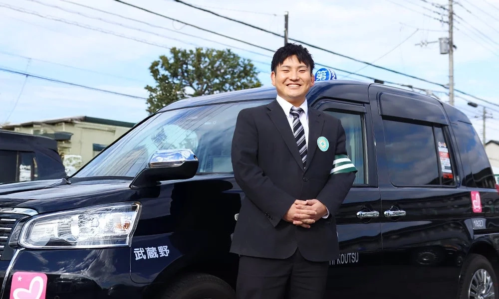 黒いタクシーの前に立つ笑顔の男性運転手