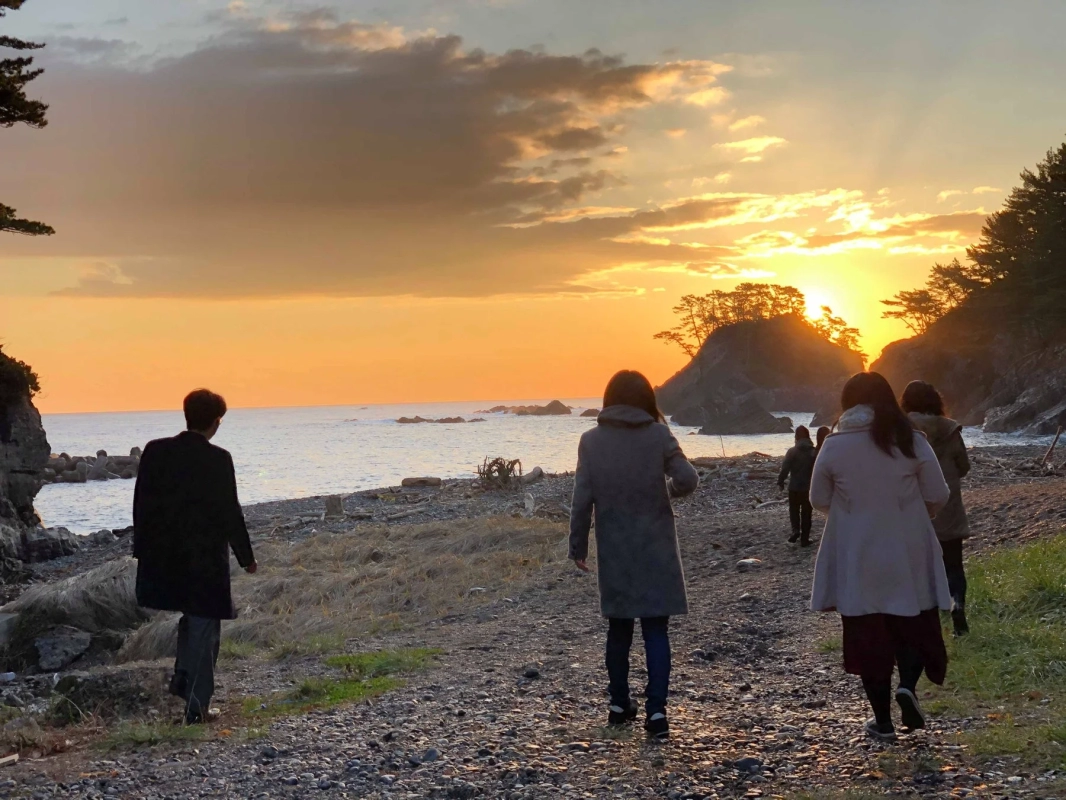 夕焼けの海岸を歩く人々の後ろ姿