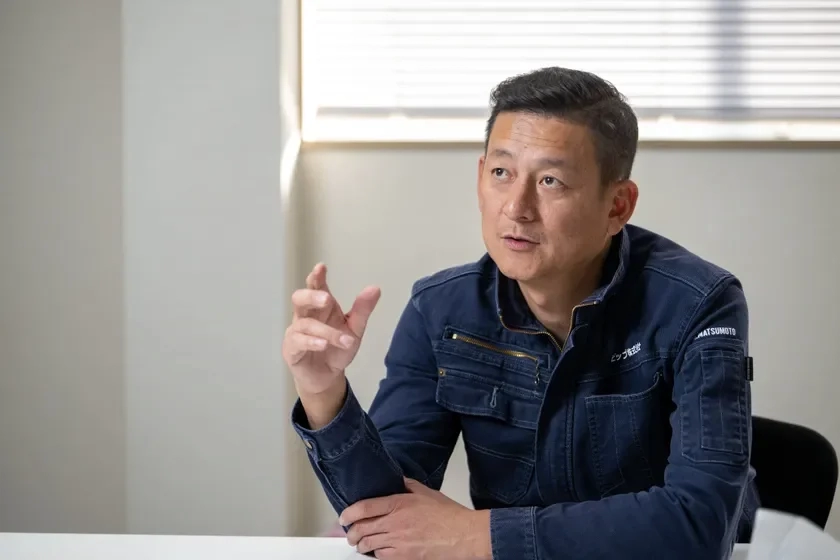 紺色の作業服を着て話す代表取締役 松本勝さん