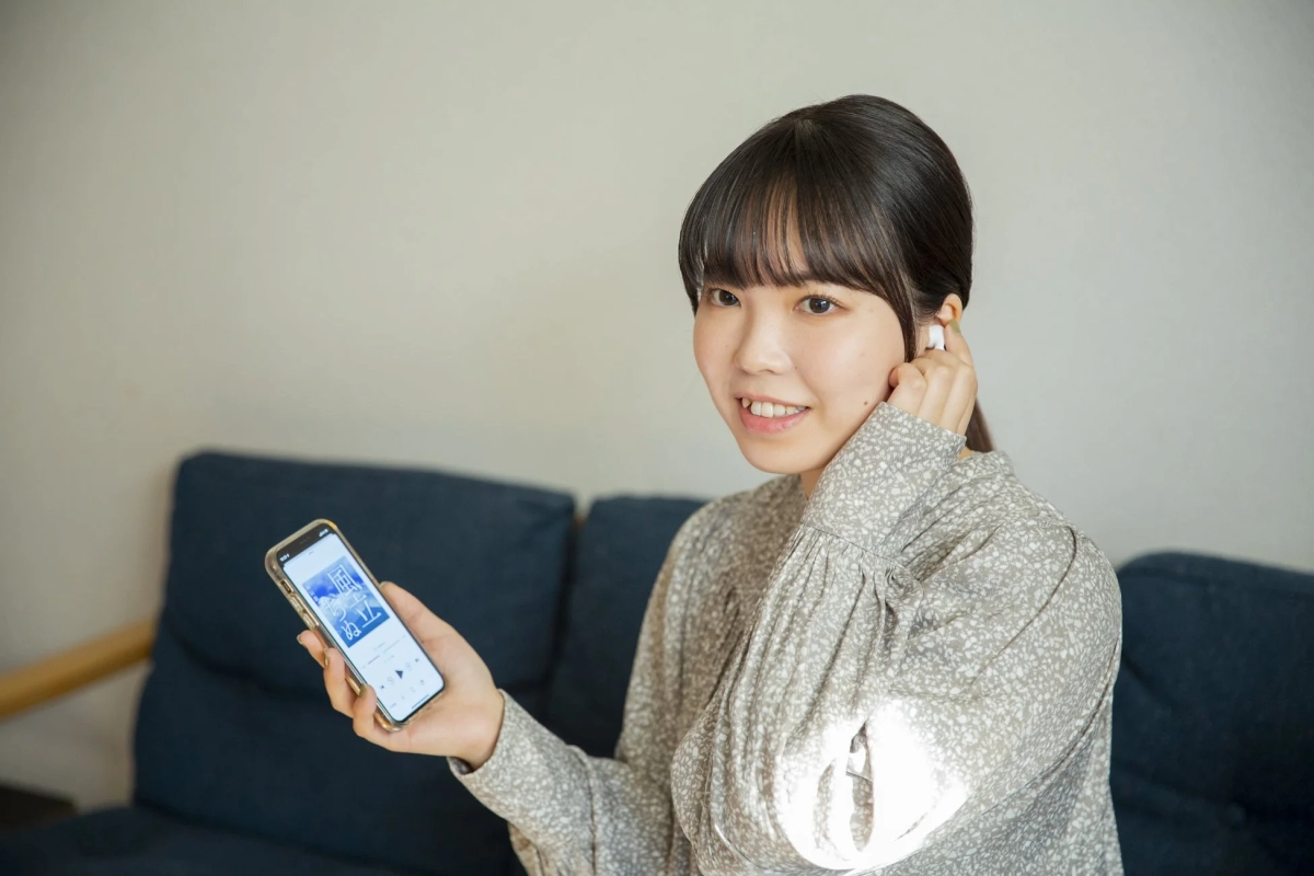 ソファに座ってワイヤレスイヤホンでスマホを操作する女性