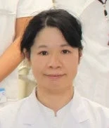 白衣を着たアジア系の女性がカメラをまっすぐ見ています。彼女は真面目な表情をしており、医療または研究分野の専門家のように見えます。