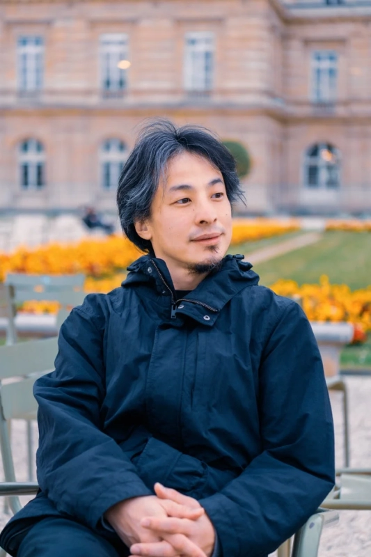 紺色のジャケットを着た男性が屋外の公園で椅子に座っているポートレート